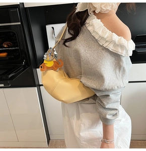 Detail of yellow leather croissant bag with an orange elephant charm in a home setting