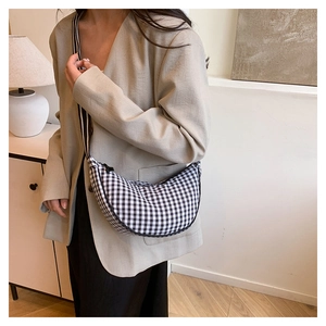 Detail of checkered crescent bag with striped strap worn with a beige blazer coat