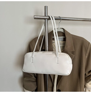 White faux leather baguette bag with dual handles hanging on a suit in a studio setting