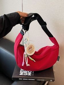Red nylon hobo bag with wide black strap and capybara charm accessory for women