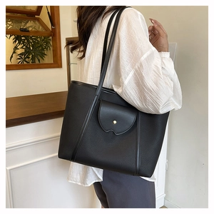 Close-up of black lychee grain tote bag with gold snap button on shoulder of model