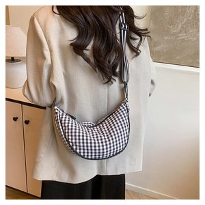 Detail of checkered crescent bag with striped wide shoulder strap on model in beige blazer