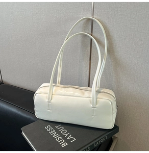 Detail shot of a minimalist white glossy PU leather shoulder bag on a business book