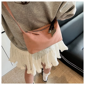 Detailed shot of pink suede shoulder bag featuring a romantic heart-shaped metal pendant