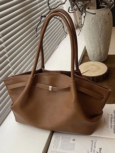 Brown leather tote bag with decorative buckle strap and long shoulder handles in warm light