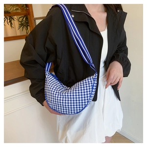 Detail of blue gingham crossbody bag with adjustable striped strap on model