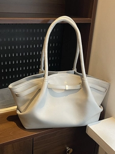 Minimalist beige leather tote bag with elegant folds on dark wooden shelf display