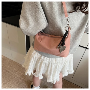 Detail of pink faux suede crossbody bag featuring a silver heart-shaped metal pendant