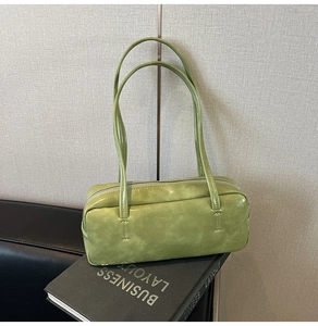 Detailed shot of a green leather baguette bag resting on a book in a stylish interior