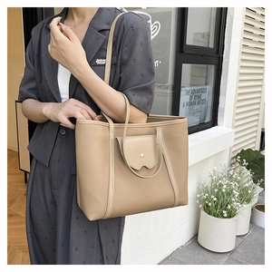Detail shot of a beige leather tote bag with lychee texture and front pocket on a model