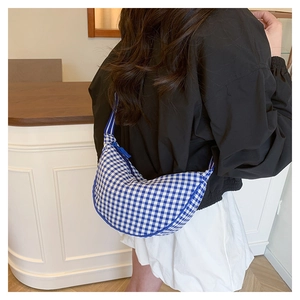 Rear view of a blue and white checkered crescent crossbody bag worn by a model in a cafe