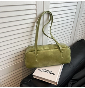 Close-up of grass green faux leather shoulder bag on a sofa with decorative books