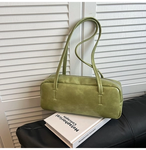 Detail of light green leather baguette bag on white book with minimalist shoulder straps