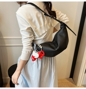 Detail view of a black crescent crossbody bag with a decorative red elephant charm accessory