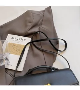 Detail of a black leather handbag with smooth long shoulder strap and gold clasp