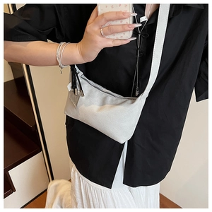Detail of white minimalist crossbody bag with heart pendant on model in natural light