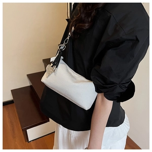 Minimalist white crossbody bag with black knotted strap and silver heart pendant detail