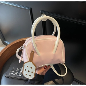 Detail of pink and white contrast handbag with artist palette charm on a wood chair