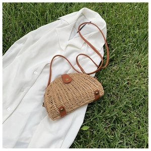 Close-up of woven straw saddle bag with brown leather flap and bronze metal studs