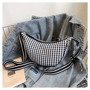 Detail of checkered crescent crossbody bag on denim jacket with striped strap