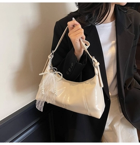 Detail of off-white glossy hobo bag featuring pearl lace bow and adjustable strap