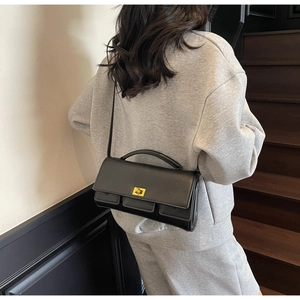 Detail of a black leather baguette bag with gold buckle worn by a model in casual style