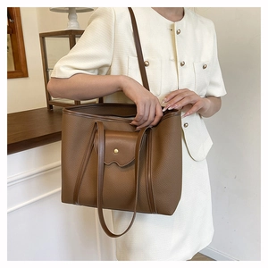 Close-up of brown pebbled leather tote bag featuring a front pocket with gold metal buckle