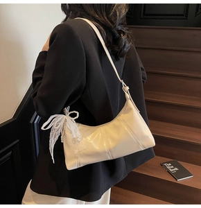Side view of creamy white patent leather hobo bag with lace bow and pearl charm detail