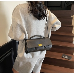 Detail of a black rectangle bag with gold hardware and top handle in a lifestyle setting