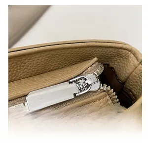 Detail view of khaki pebbled leather bag featuring a smooth silver metal zipper closure