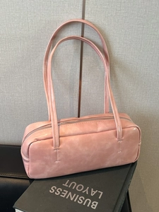 Pink rectangular leather shoulder bag with zipper closure shown on a desk background