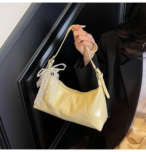 Detail of light yellow crossbody bag featuring lace bow decoration and pearl pendant