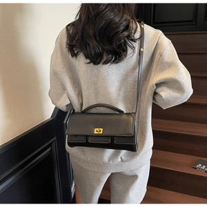 Detail of a black leather square bag featuring a gold twist-lock and top handle strap