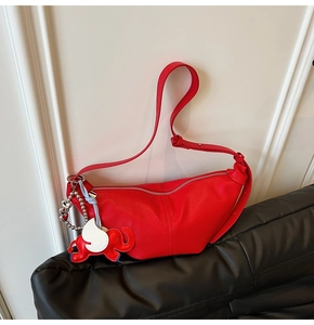 Detail of red litchi leather dumpling bag with elephant charm on black sofa