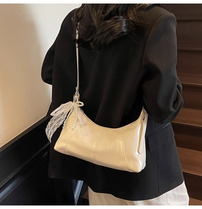 Detail of cream white leather hobo bag with lace bow and pearl charm on a model