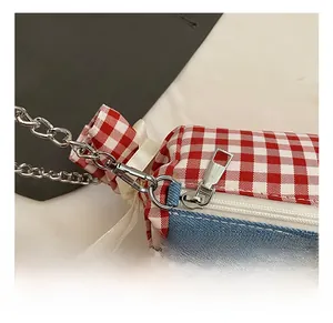 Detail of high-gloss silver metal hook and chain on a plaid and denim handbag