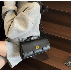 Detail of black satchel bag with golden lock and dual front pockets on model