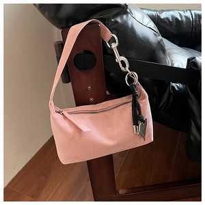 Detail of pink suede pillow bag with silver chain strap and heart charm on a wooden chair