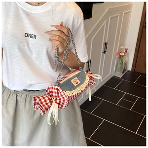 Detail of candy-shaped red gingham crossbody bag with lace accents and silver chain strap