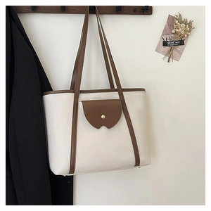 Detail of large tote bag with brown leather pocket and gold button on textured white base
