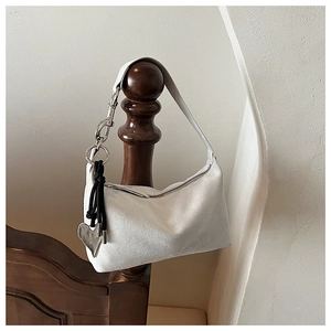 Detail of white suede pillow bag with silver rings and heart charm on wooden pole