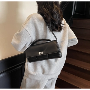 Model wearing black leather crossbody bag with silver buckle on minimalist stairs