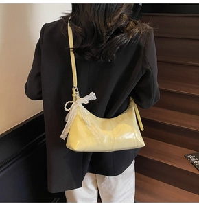 Detail of light yellow glossy shoulder bag with a lace pearl bow on a model side