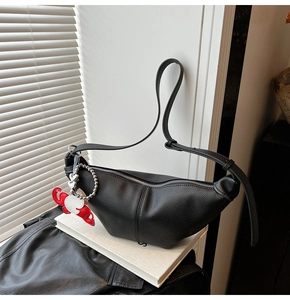 Detail of black litchi texture crescent bag with heart pendant on white book