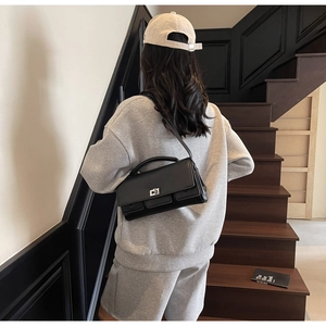 Detailed view of black minimalist leather handbag featuring silver square rotary lock