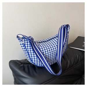 Detail of blue and white checkered crescent bag with adjustable nylon strap on bench