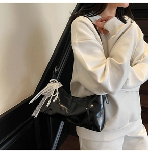Detailed view of black glossy shoulder bag featuring a pearl and lace bow charm detail