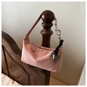 Detail of pink suede pillow bag with silver heart pendant on a wooden post