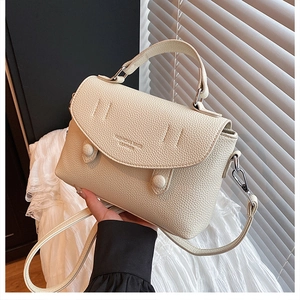Detail of cream lychee texture leather handbag with gold lettering and adjustable strap