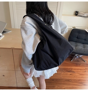 Detail view of large black tote bag with wide shoulder strap and matte nylon fabric texture